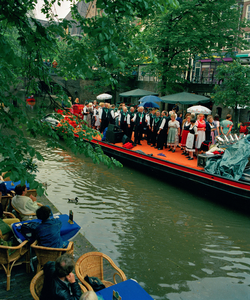 840362 Afbeelding van een zangkoor dat zingt op een 'muziekboot' op de Oudegracht bij de Jansbrug te Utrecht, tijdens ...